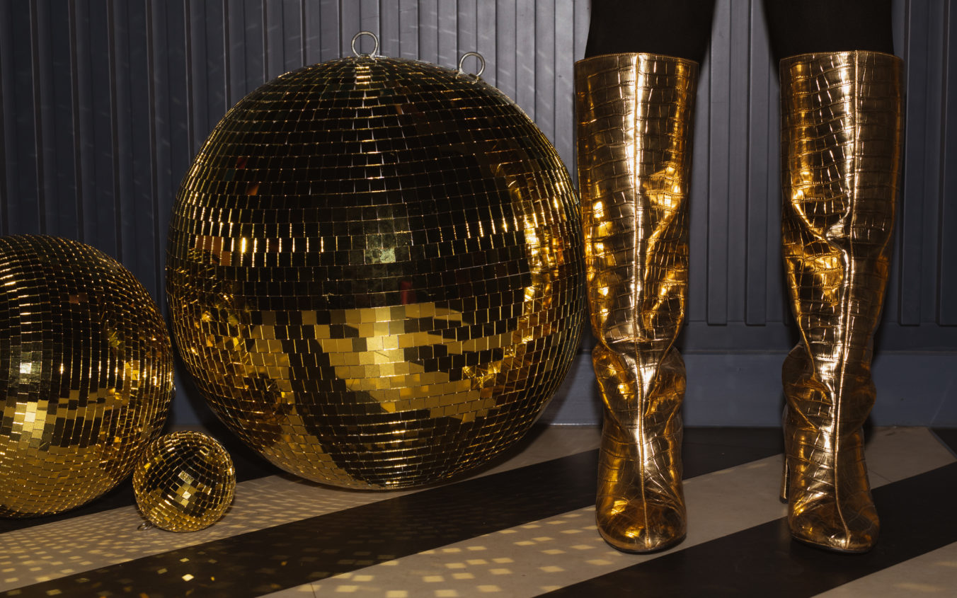 Woman in gold boots next to golden disco balls